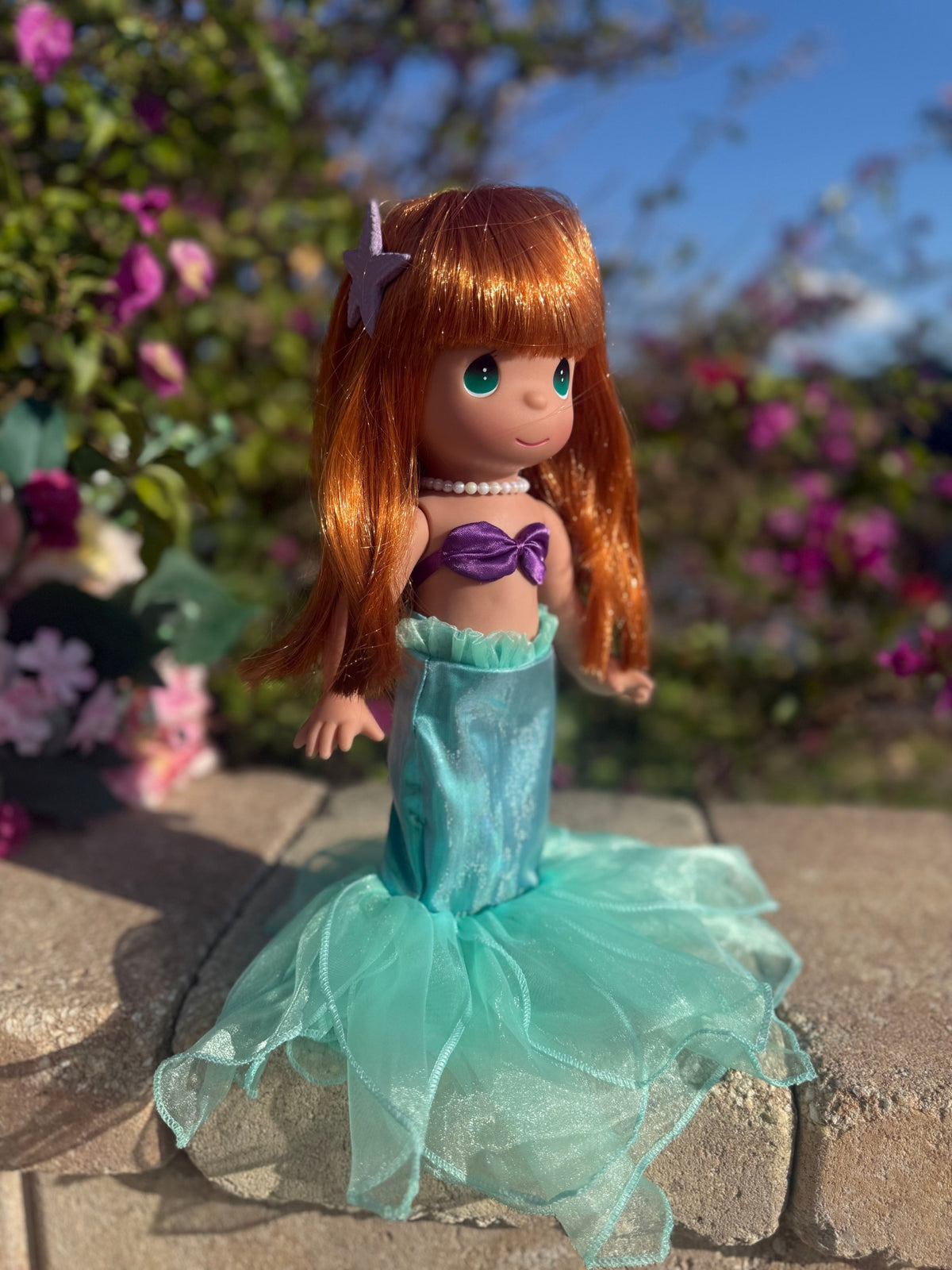 The Doll Maker 12-inch Ariel mermaid doll with red hair, purple seashell top, and turquoise tulle tail outdoors.