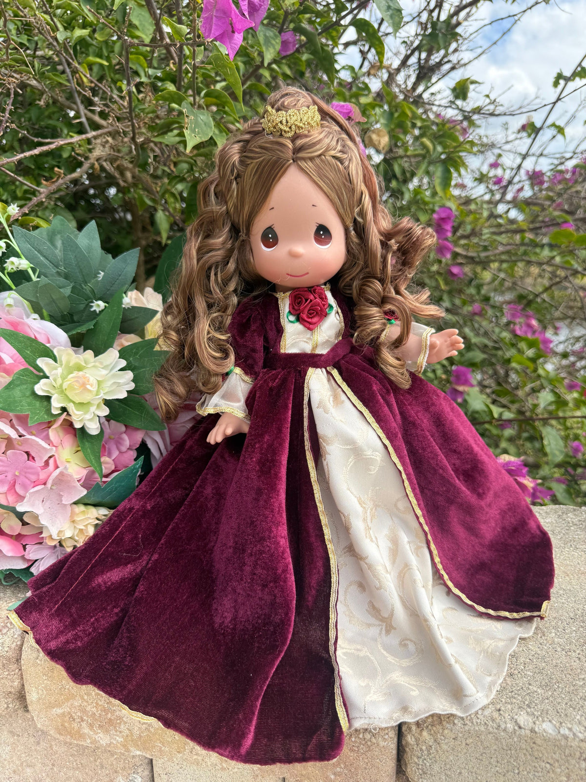 The Doll Maker 12-inch Belle Christmas doll wearing a burgundy velvet gown with gold trim and a small gold crown.