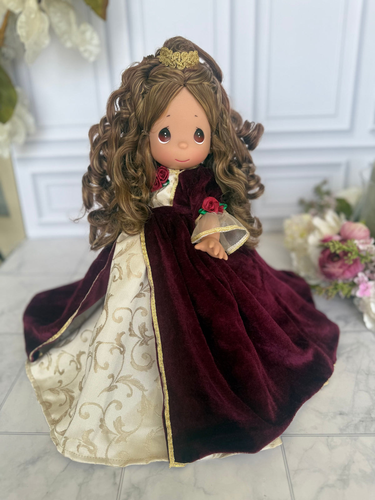 The Doll Maker 12-inch Belle Christmas doll wearing a burgundy velvet gown with gold floral accents and a gold crown.