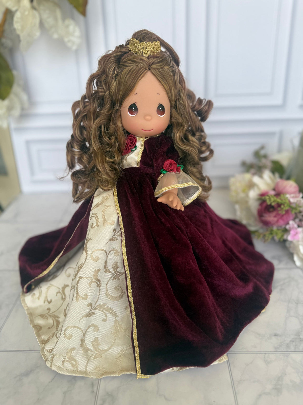 The Doll Maker 12-inch Belle Christmas doll wearing a burgundy velvet gown with gold floral accents and a gold crown.