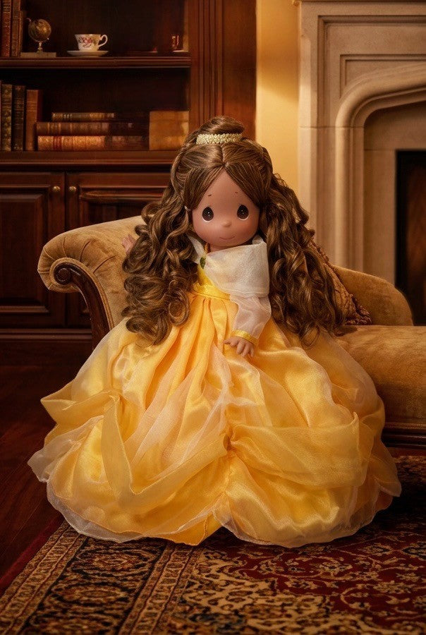 The Doll Maker 12-inch Belle vinyl doll wearing an iconic yellow gown with elegant draping, seated on a velvet chair.