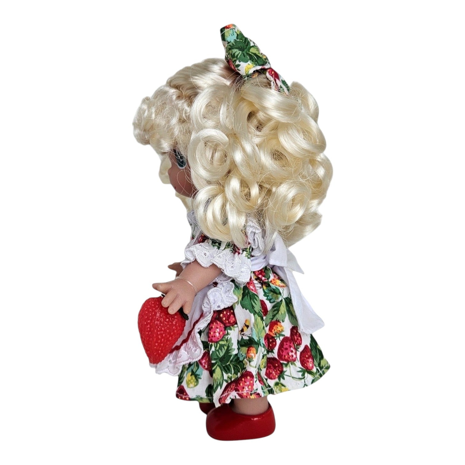 The Doll Maker 9-inch You’re Berry Sweet vinyl doll with blonde curls, wearing a strawberry print dress and red shoes.