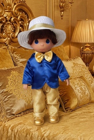 The Doll Maker 50th anniversary Bert doll in a blue jacket, gold trousers, and white hat on a gold bedspread.
