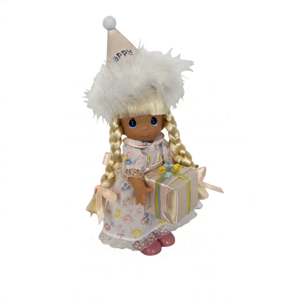The Doll Maker 7-inch blonde vinyl birthday doll wearing a floral dress, party hat, and holding a gift box