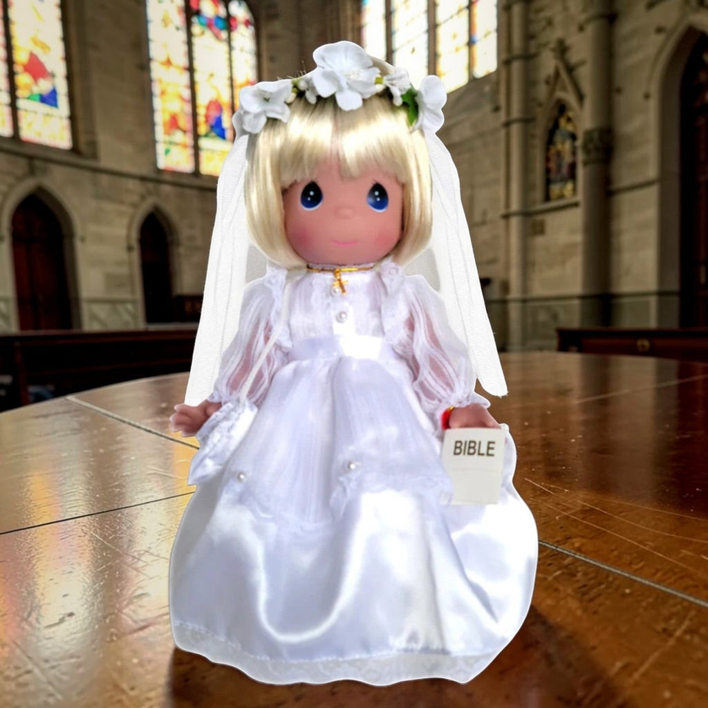 The Doll Maker 12-inch blonde communion doll wearing a white satin gown, veil, flower crown, and gold cross necklace.