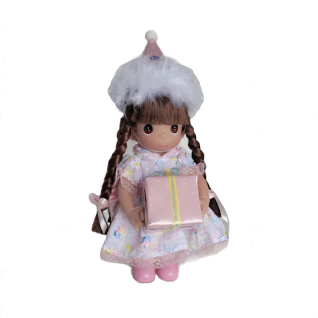 The Doll Maker 7-inch brunette birthday doll wearing a pink party hat with fur trim and a floral dress holding a gift