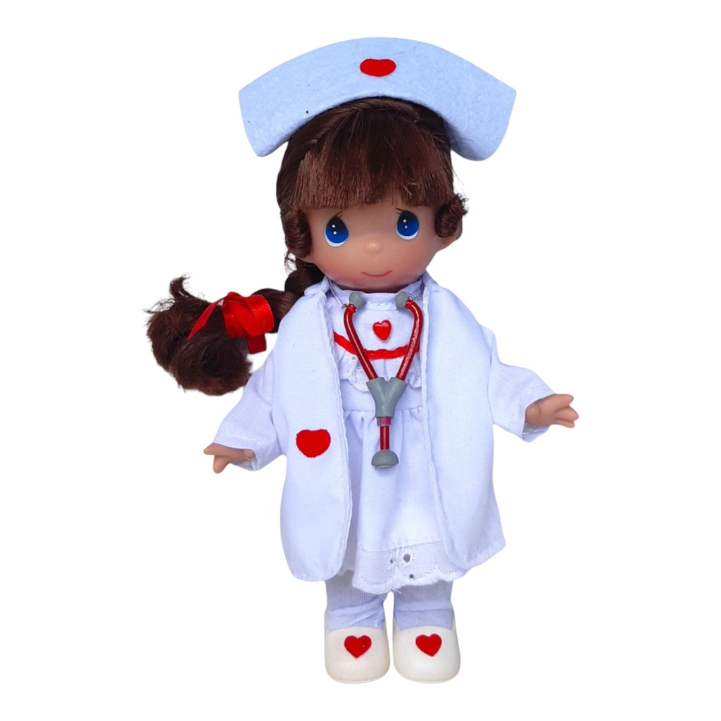 The Doll Maker Loving Touch Nurse 7-inch brunette vinyl doll wearing a white nurse uniform with red heart accents.