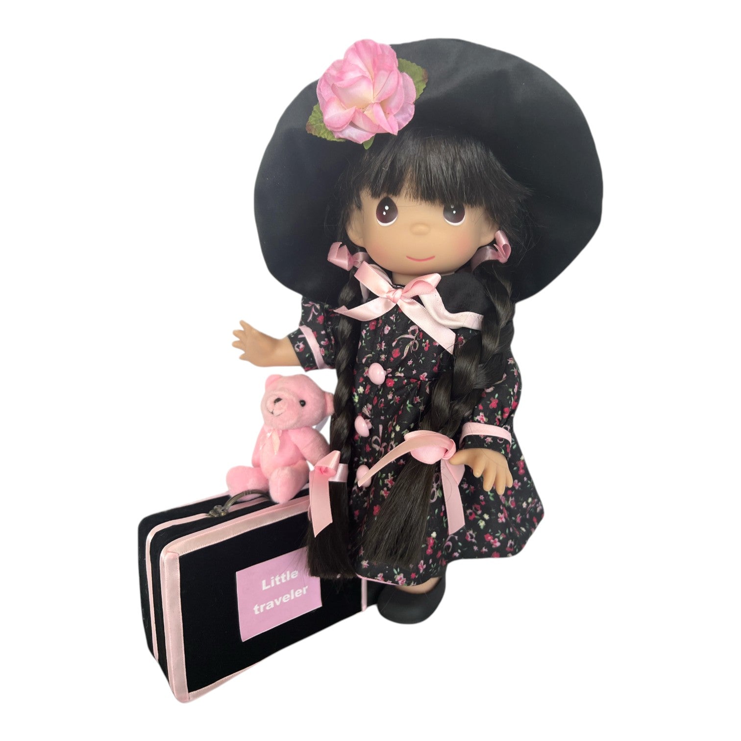 The Doll Maker 12-inch brunette vinyl doll wearing a floral dress, black hat, and pink ribbons with a suitcase and bear
