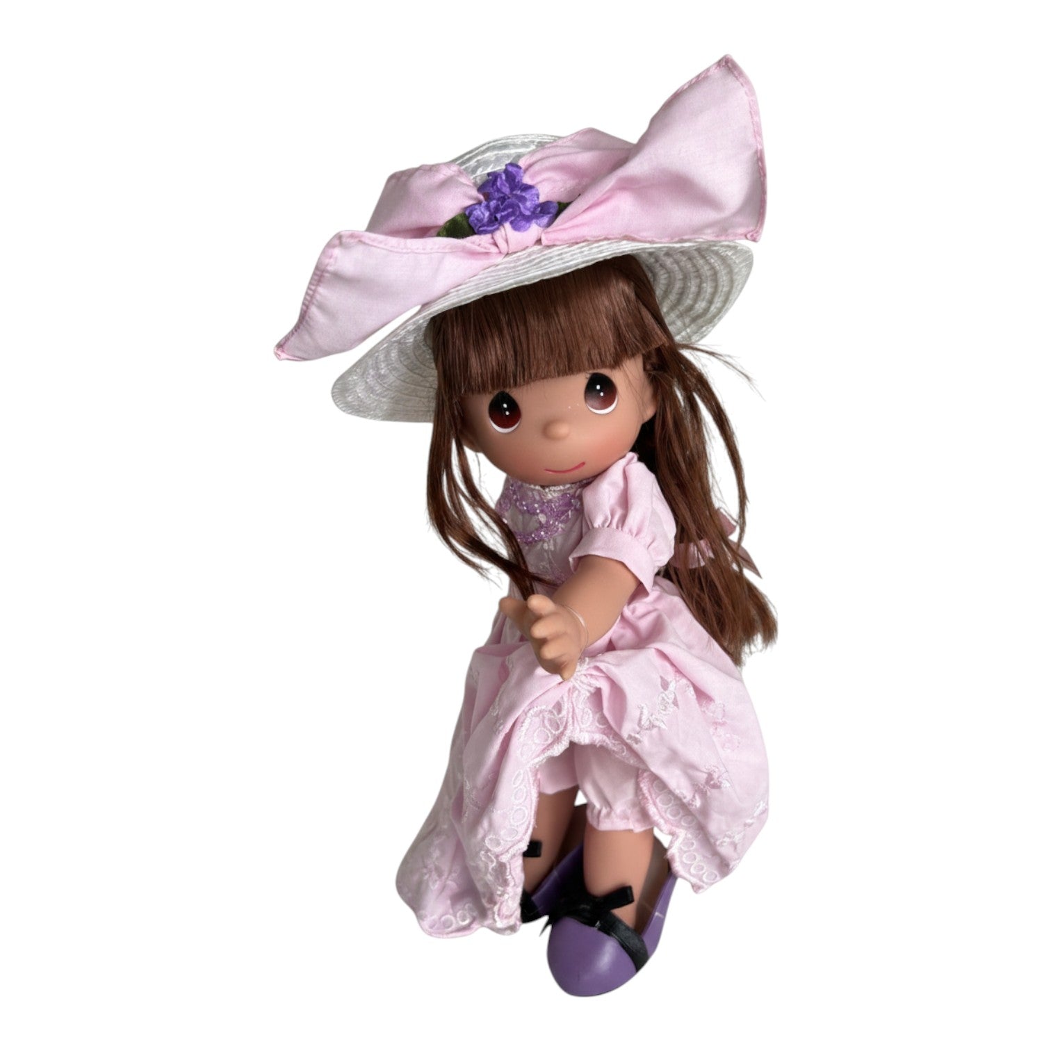 The Doll Maker 12-inch brunette Precious Moments doll wearing a pink dress, pink necklace, and oversized purple shoes.