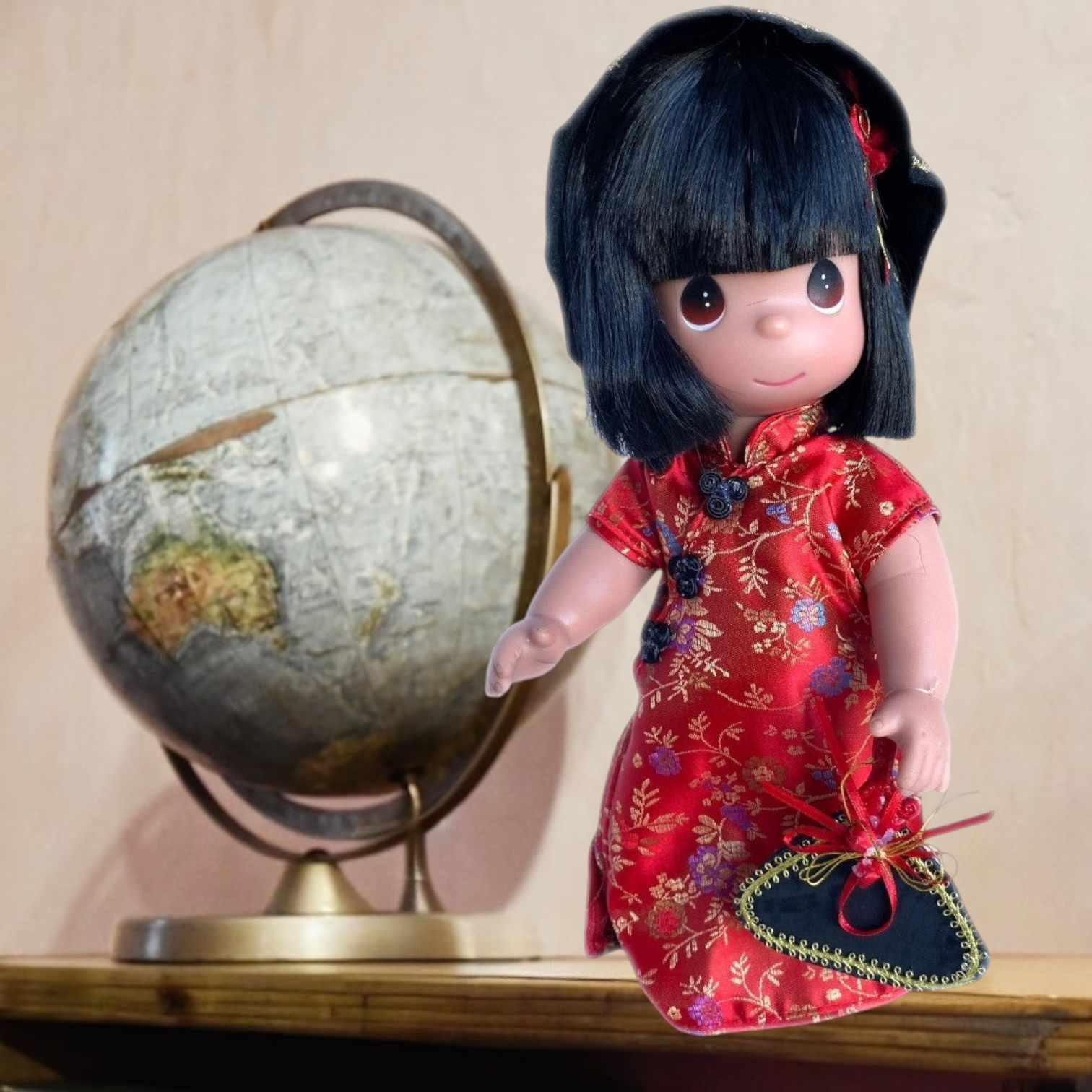 The Doll Maker 12-inch China collectible doll in a red floral dress with black hat and fan, standing by a globe.