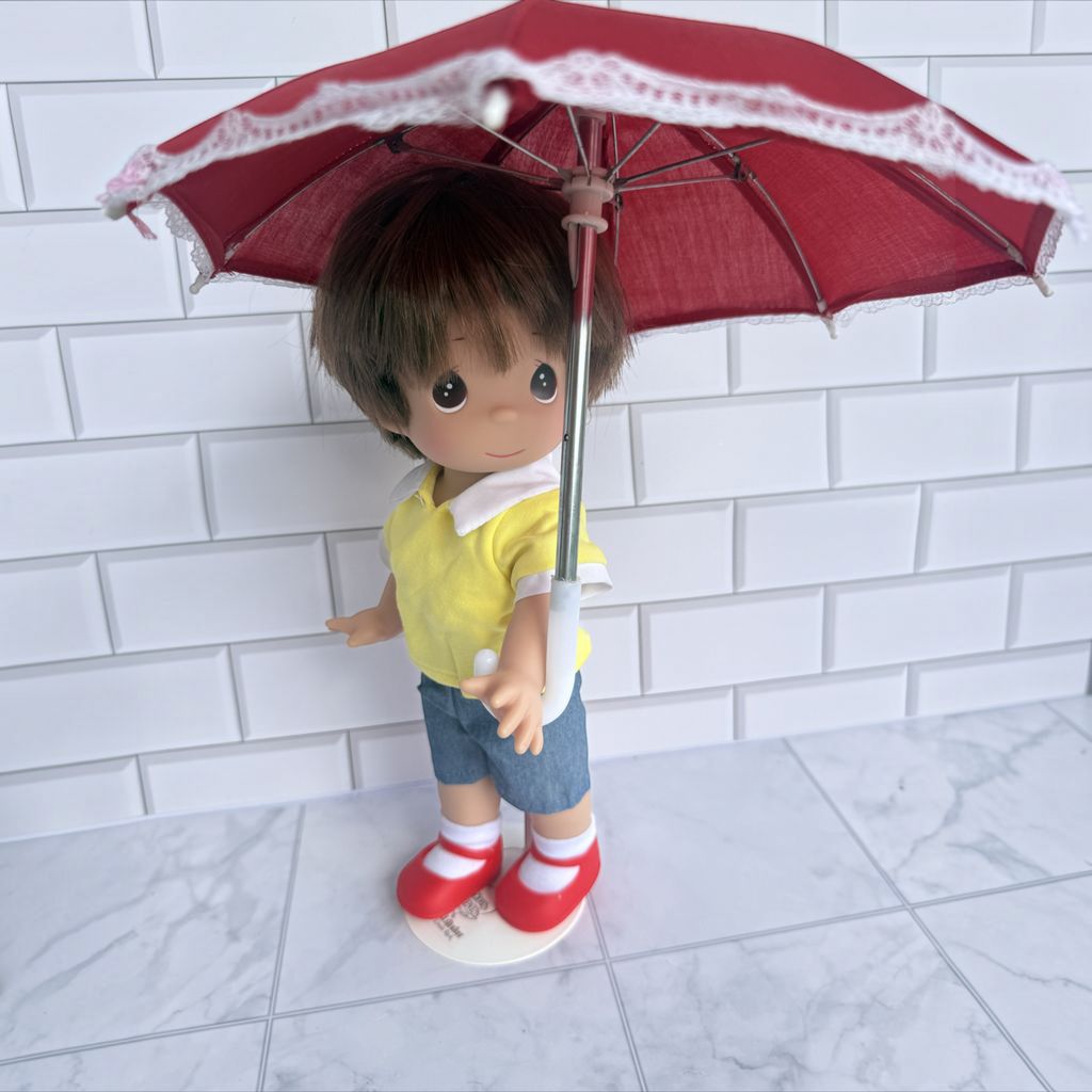 The Doll Maker 12-inch Christopher Robin doll wearing a yellow shirt and blue shorts, holding a red lace umbrella.