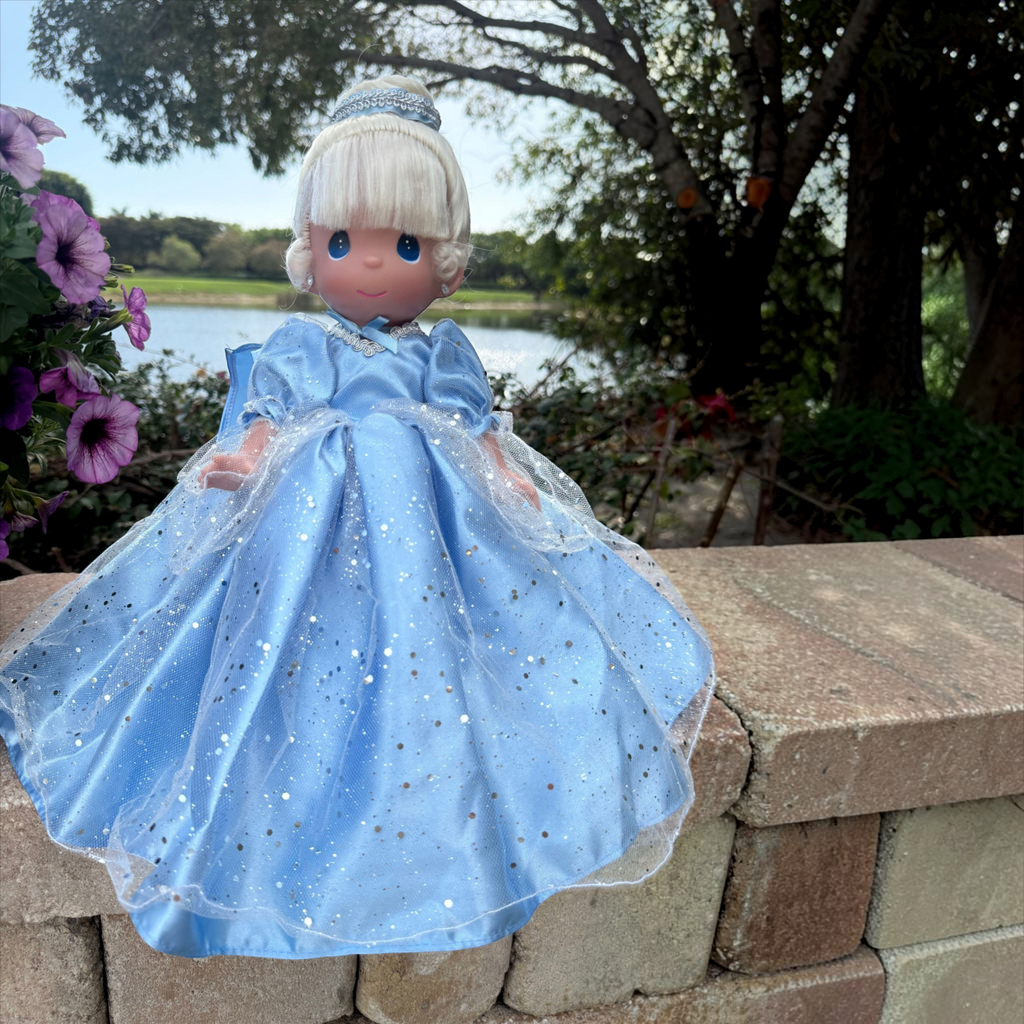 The Doll Maker 12-inch Cinderella vinyl doll wearing a sparkling blue gown with a tulle overlay, posed outdoors.