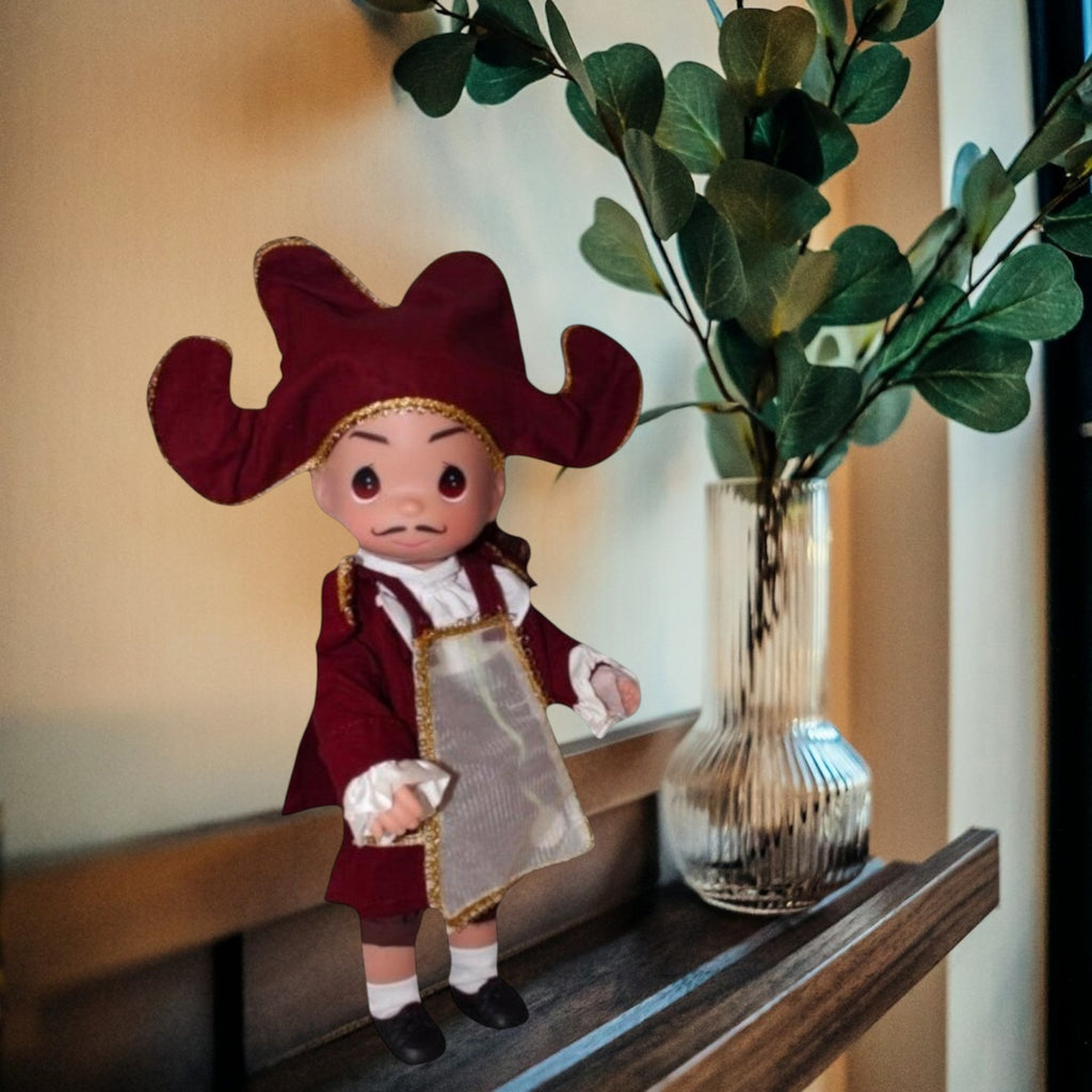 The Doll Maker 12-inch Cogsworth doll from Beauty and the Beast wearing a burgundy coat and hat with gold trim.