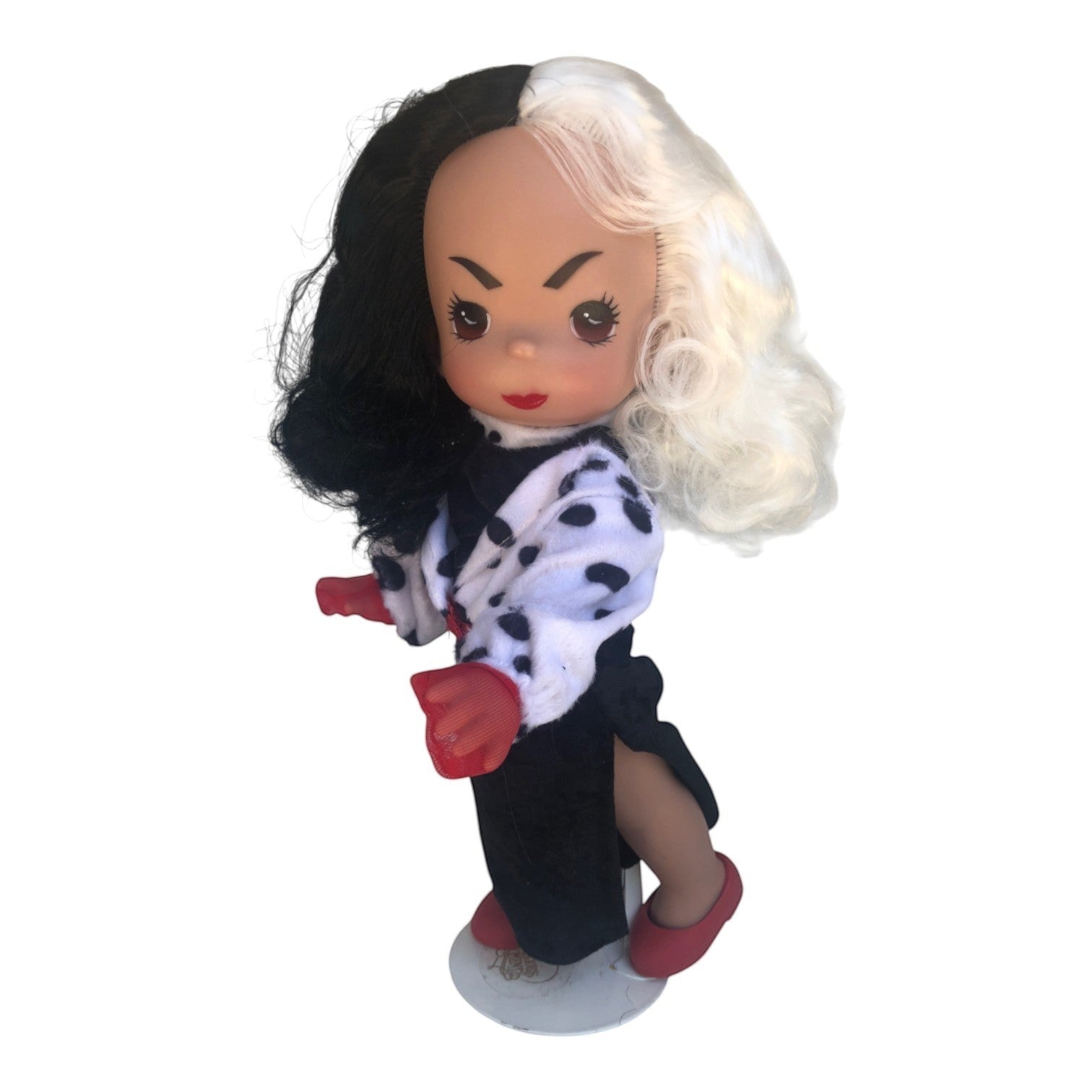 The Doll Maker 12-inch Cruella doll featuring signature black and white hair, dalmatian print coat, and red gloves.