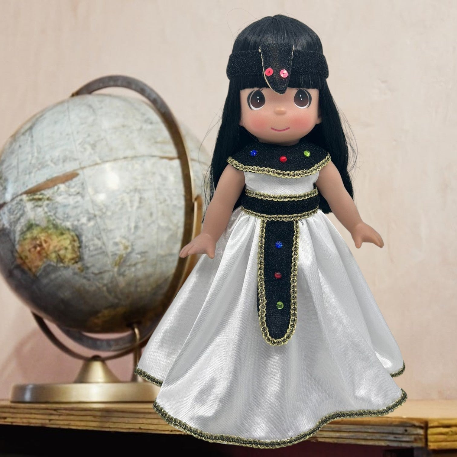 The Doll Maker 12-inch Egyptian doll with black hair, wearing a white satin dress with gold trim and jewel accents.