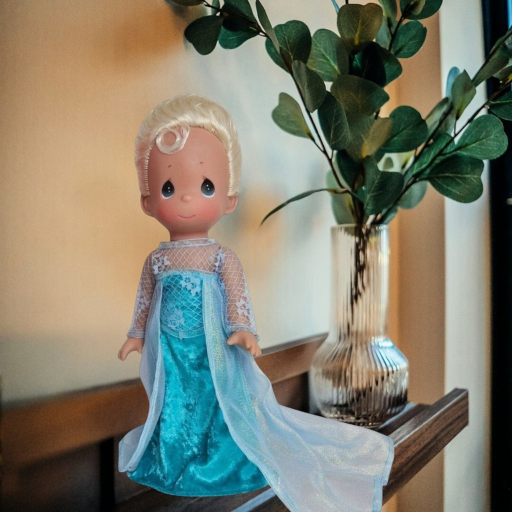The Doll Maker 12-inch Elsa doll with blonde hair wearing a signature ice-blue gown with lace and glitter details.