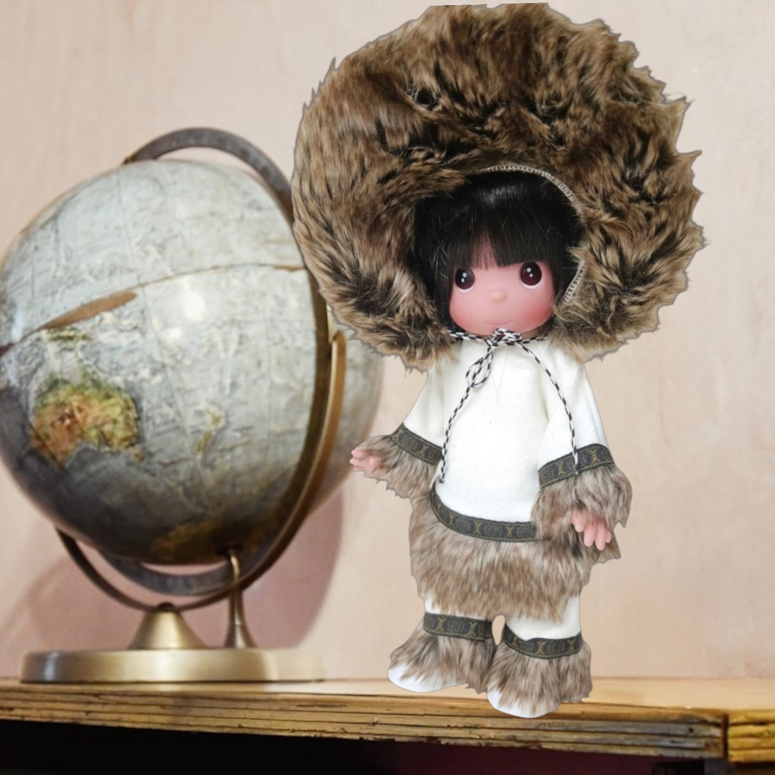 The Doll Maker 12-inch Eskimo doll wearing a white tunic and trousers with faux fur trim and a large fur-lined hood.
