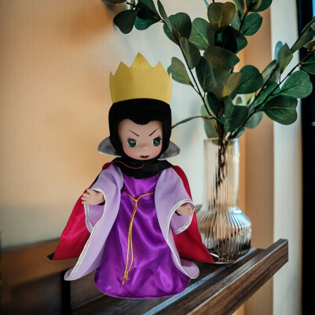 The Doll Maker 12-inch Evil Queen doll wearing a purple gown, red cape, and gold crown on a wooden shelf.