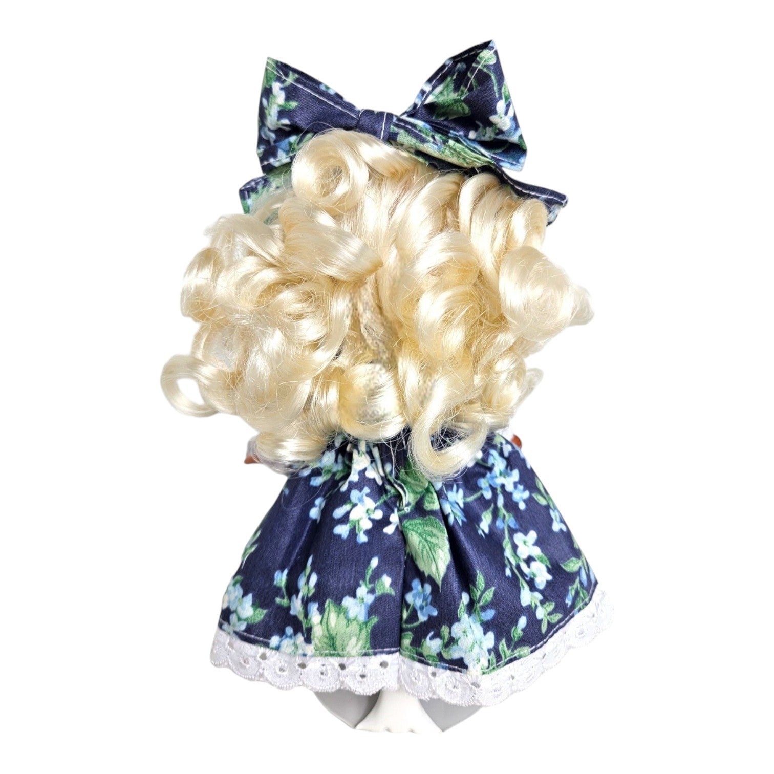 Back view of The Doll Maker Goldilocks vinyl doll with blonde curls wearing a blue floral dress and matching bow