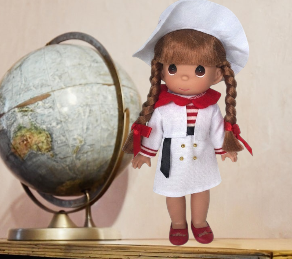 The Doll Maker 12-inch Italian girl doll wearing a white coat, red collar, and matching hat with braided hair.