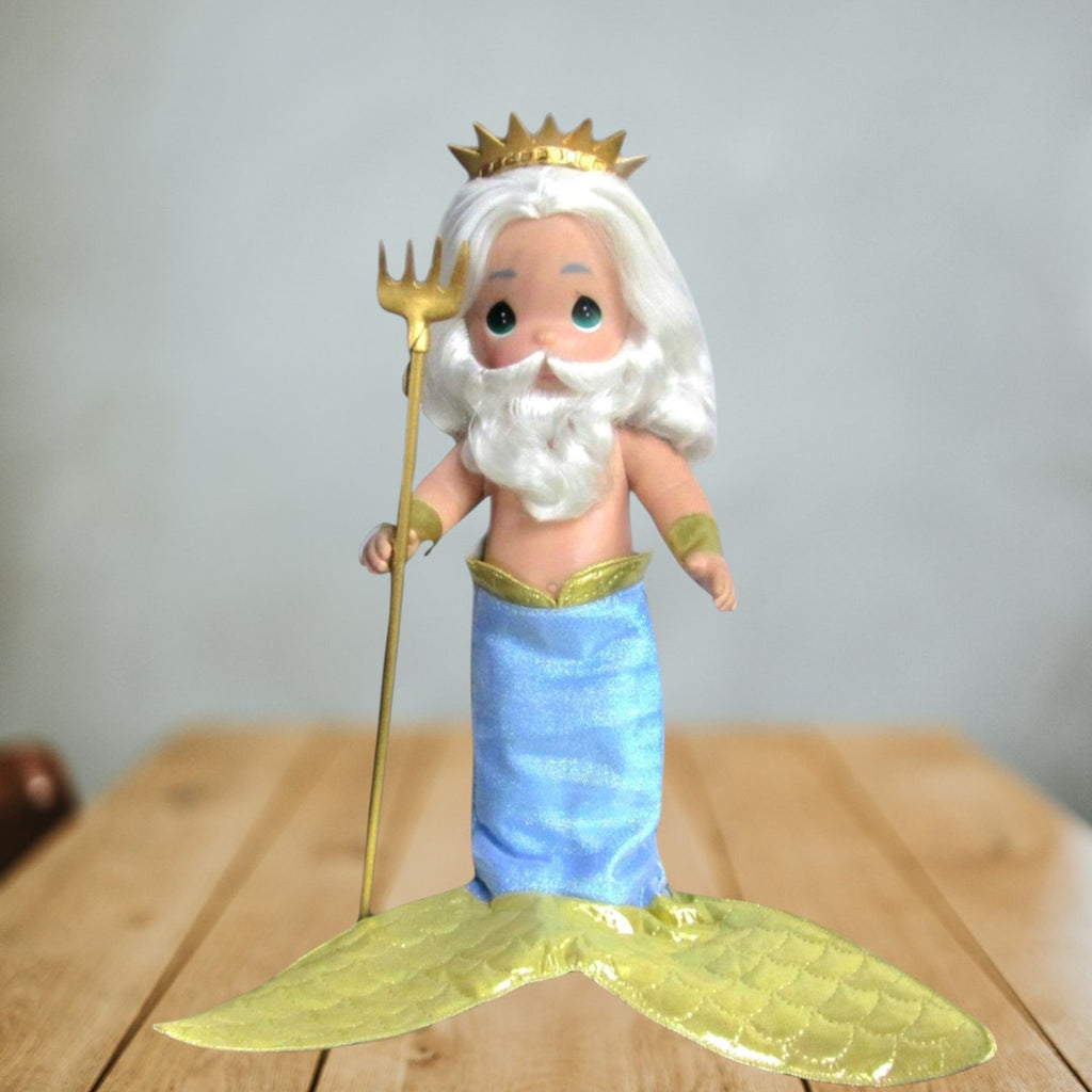 The Doll Maker 12-inch King Triton vinyl doll with white hair, gold crown, trident, and blue and gold mermaid tail.
