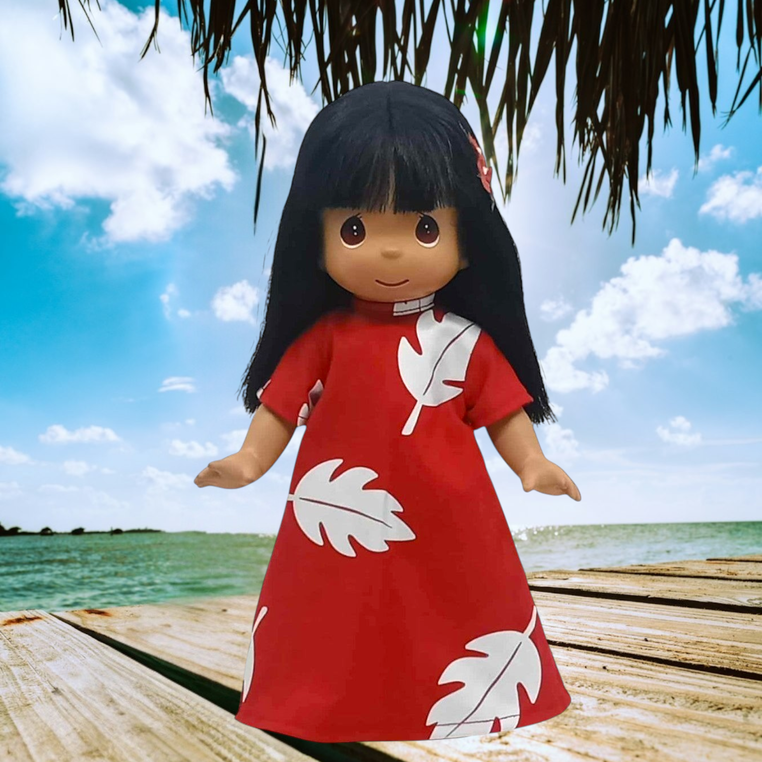 The Doll Maker 12-inch Lilo vinyl doll wearing a red dress with white leaf print, standing on a wooden dock.
