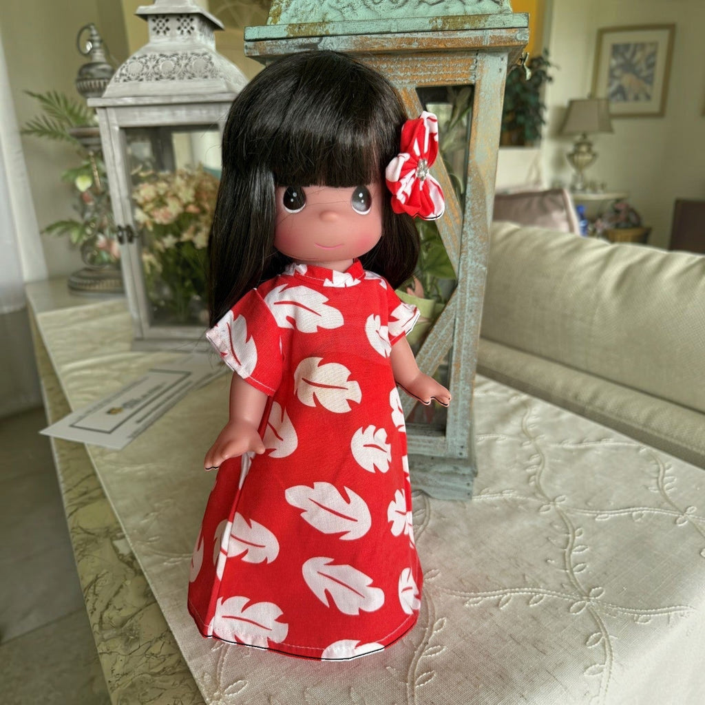The Doll Maker 12-inch Lilo vinyl doll wearing a red and white leaf-print dress with a matching hair flower accessory.