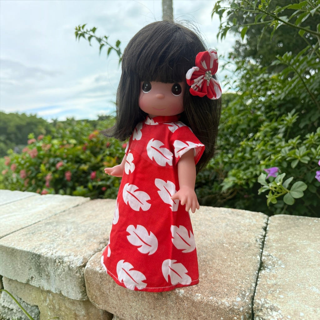 The Doll Maker 12-inch Lilo vinyl doll wearing a red and white leaf-print dress with a matching hair flower accessory.