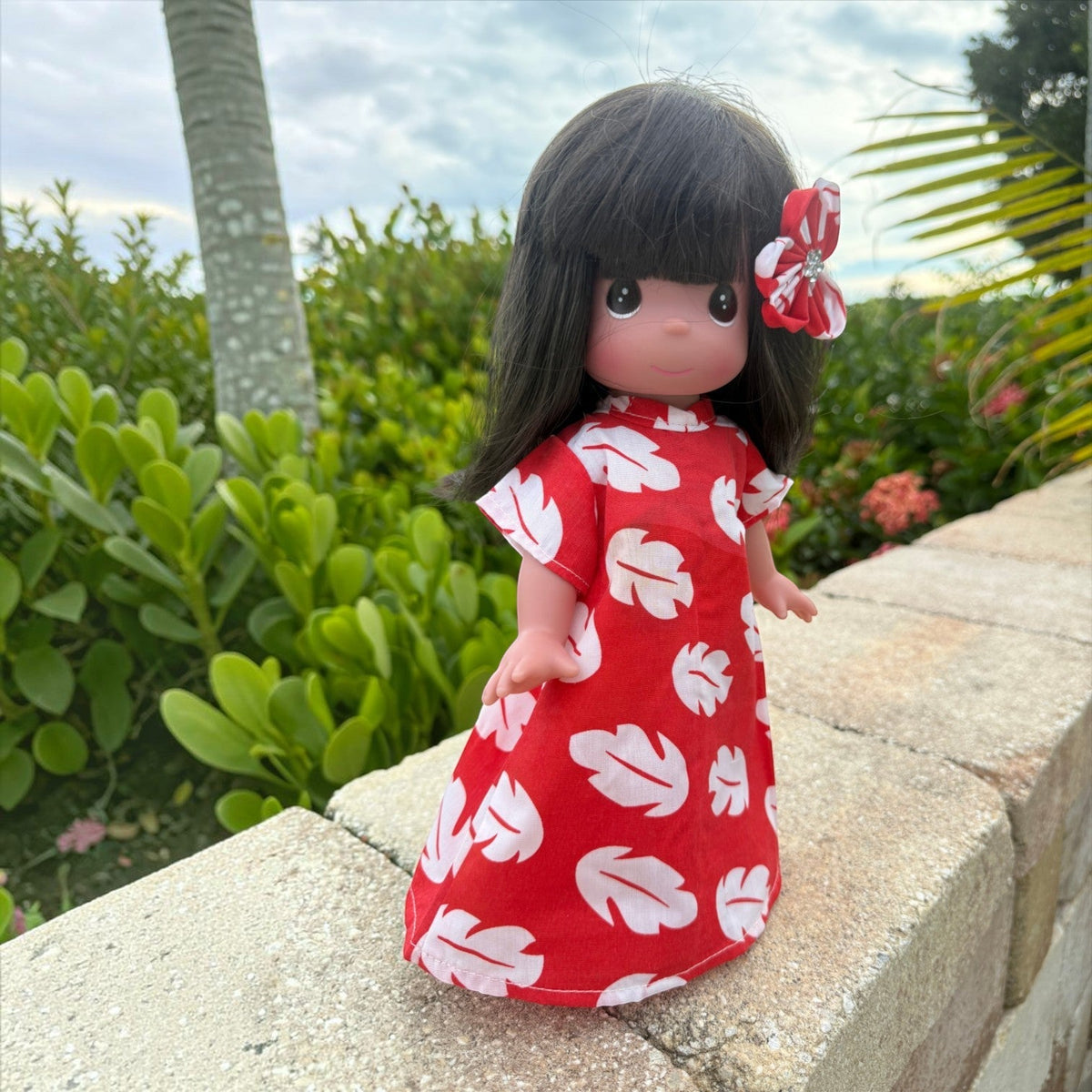 The Doll Maker 12-inch Lilo vinyl doll wearing a red and white leaf-print dress with a matching hair flower accessory.