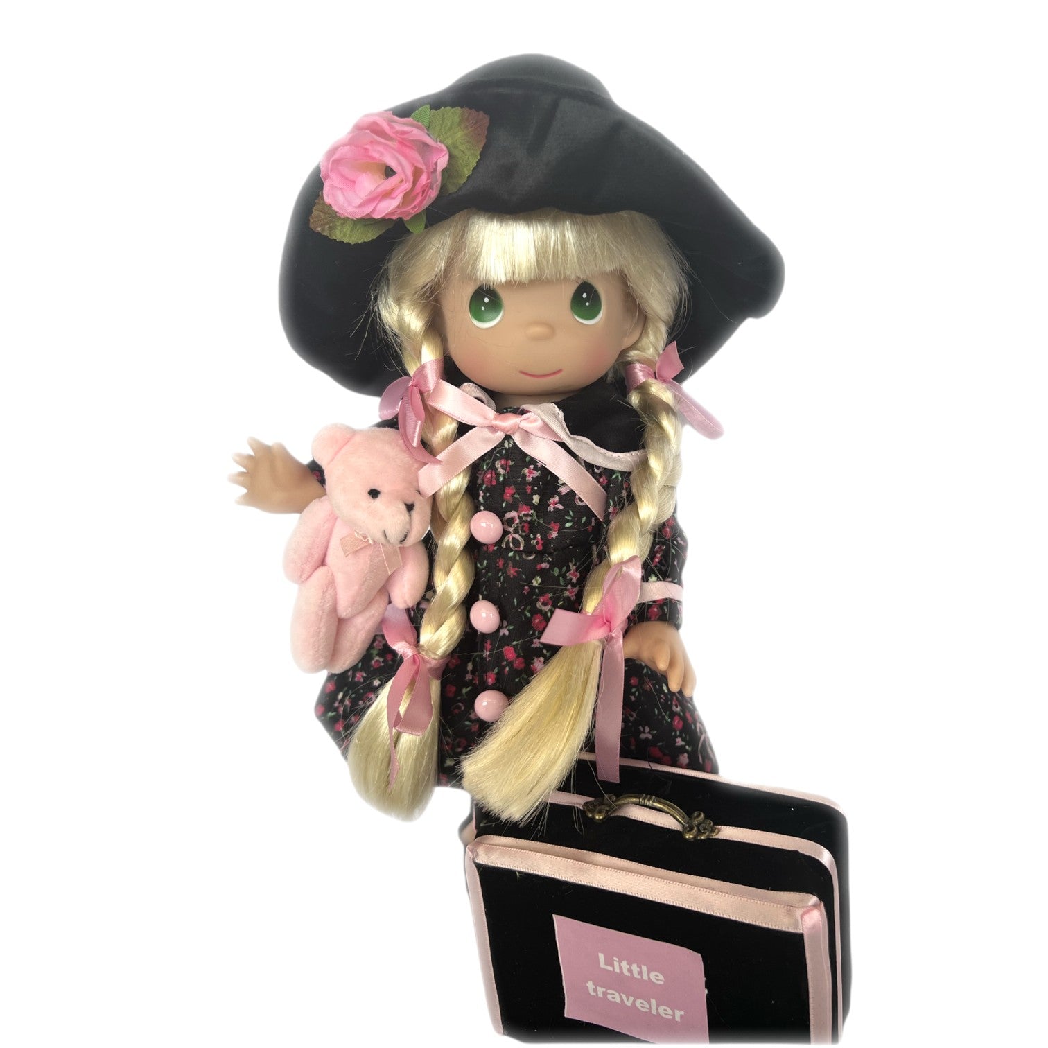 The Doll Maker Little Traveler blonde vinyl doll wearing a floral dress, black hat, and holding a pink plush bear.