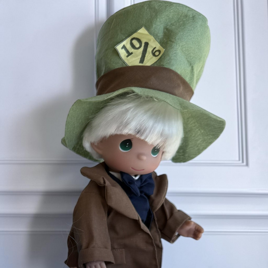 The Doll Maker Mad Hatter vinyl collectible doll wearing a large green top hat with a 10/6 price tag and brown coat.