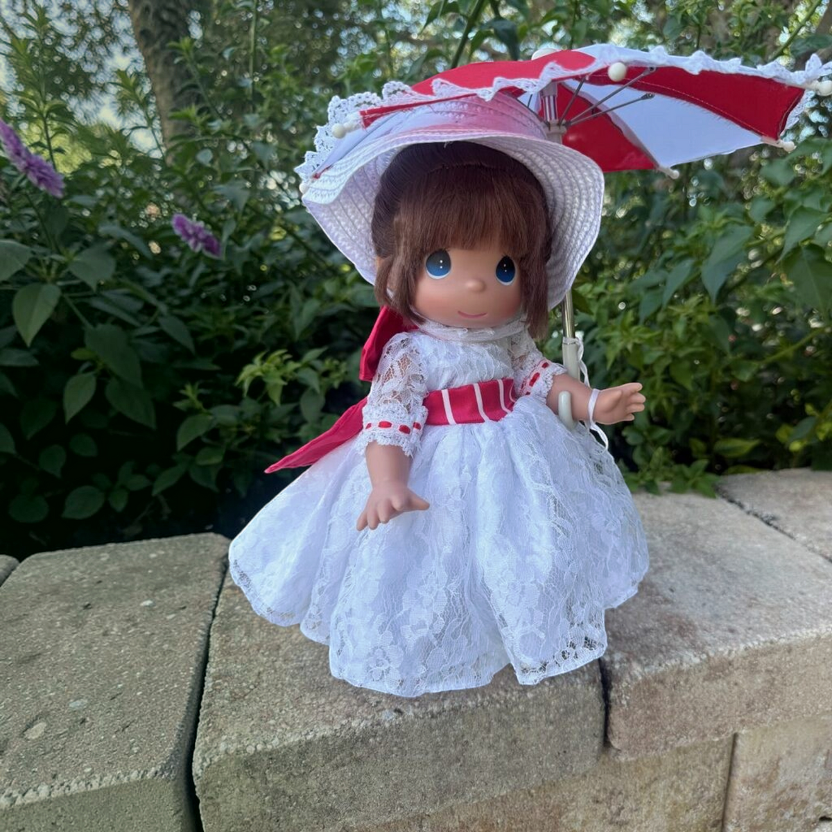 The Doll Maker 12-inch Mary Poppins doll wearing a white lace dress with red ribbons and holding a matching parasol.
