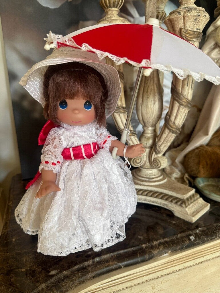 The Doll Maker 12-inch Mary Poppins doll wearing a white lace dress with red ribbons and a matching parasol.