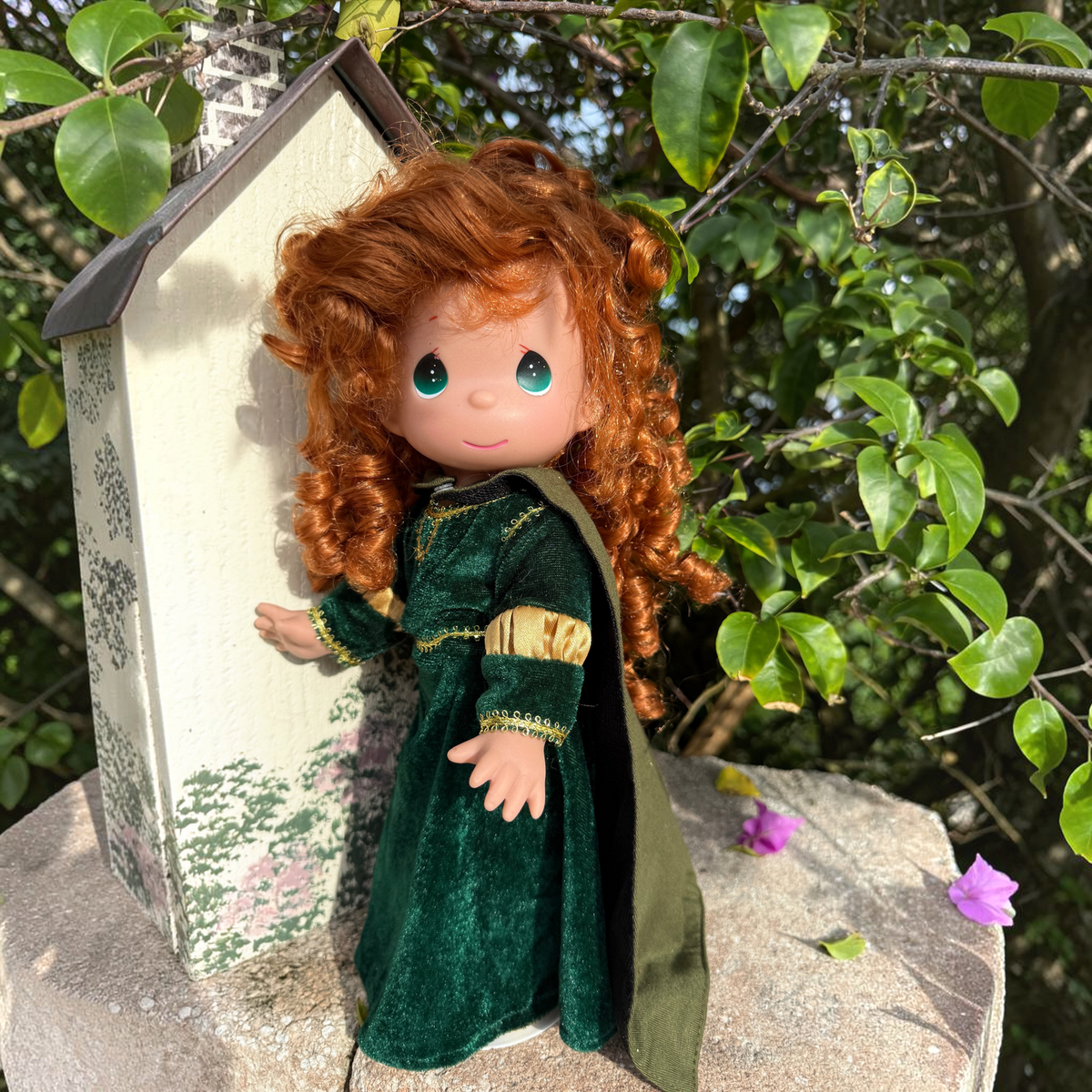 The Doll Maker 12-inch Merida doll from Brave with curly red hair wearing a green velvet dress outdoors.