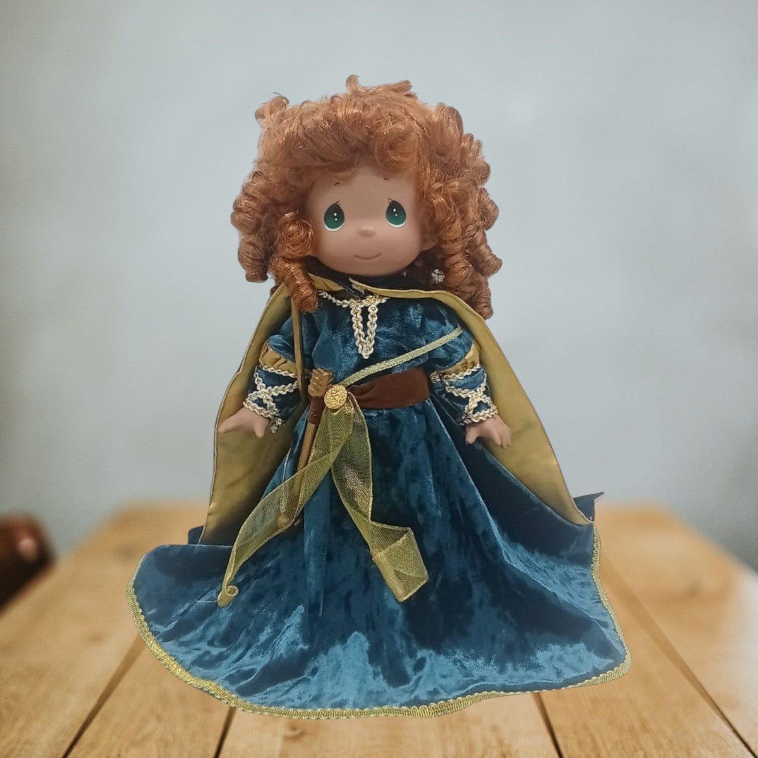 The Doll Maker 12-inch Merida vinyl doll from Brave with curly red hair wearing a teal velvet dress and gold cape.