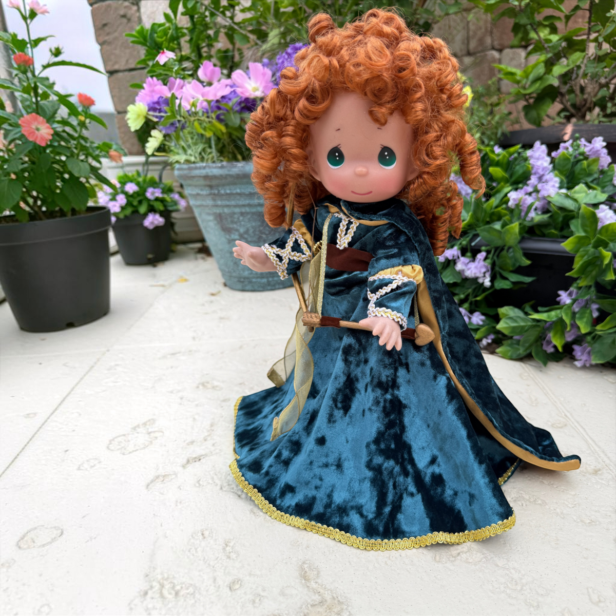 The Doll Maker Merida Brave warrior doll with curly red hair wearing a dark green velvet dress and holding a bow