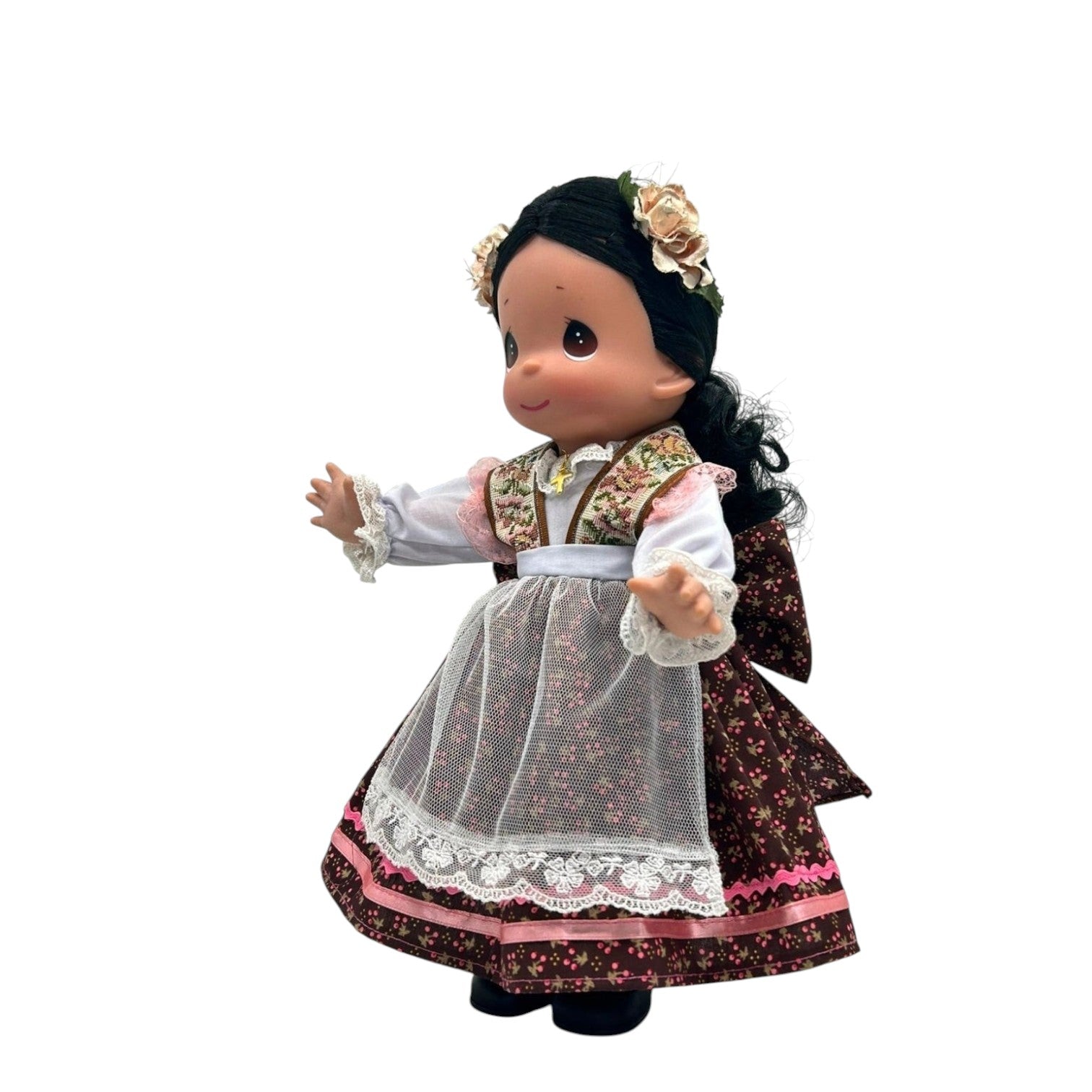 The Doll Maker 12-inch Mexico doll wearing a traditional floral dress, white apron, and flower hair accessory.