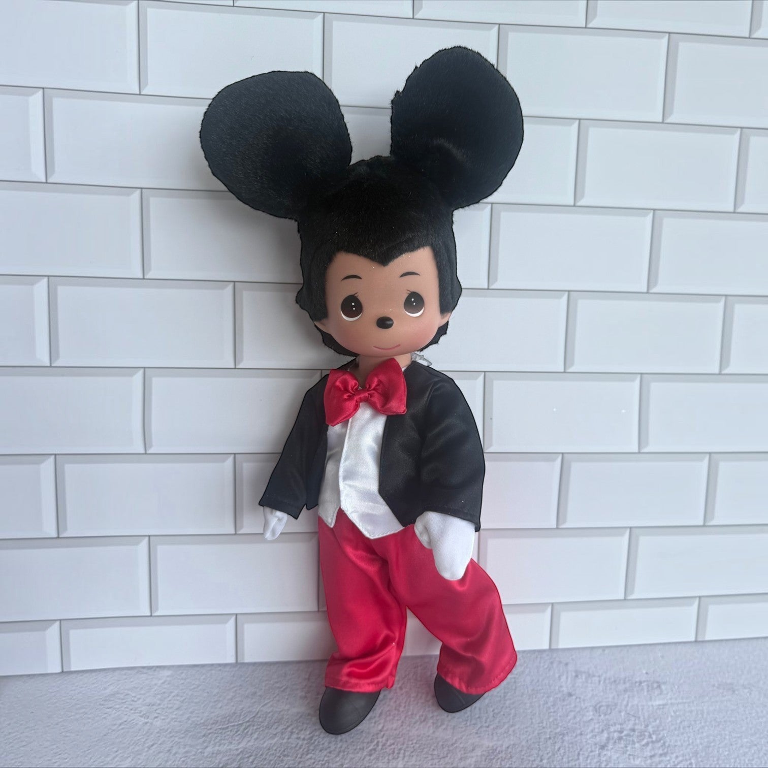 The Doll Maker 12-inch Mickey Mouse vinyl doll wearing a black tuxedo jacket, red trousers, and a red bow tie.