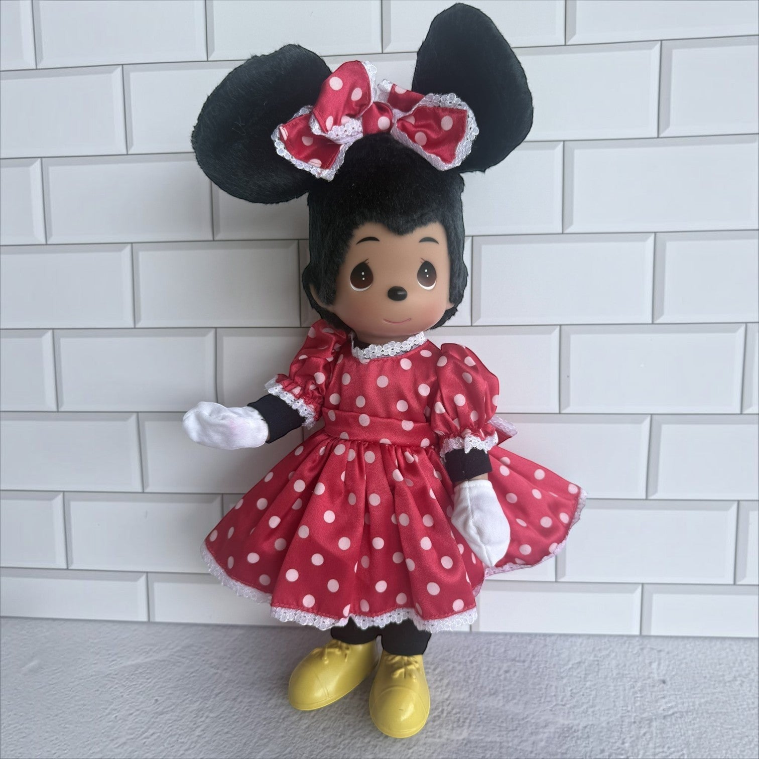The Doll Maker 12-inch Minnie Mouse vinyl doll wearing a red polka dot dress with white lace trim and yellow shoes.