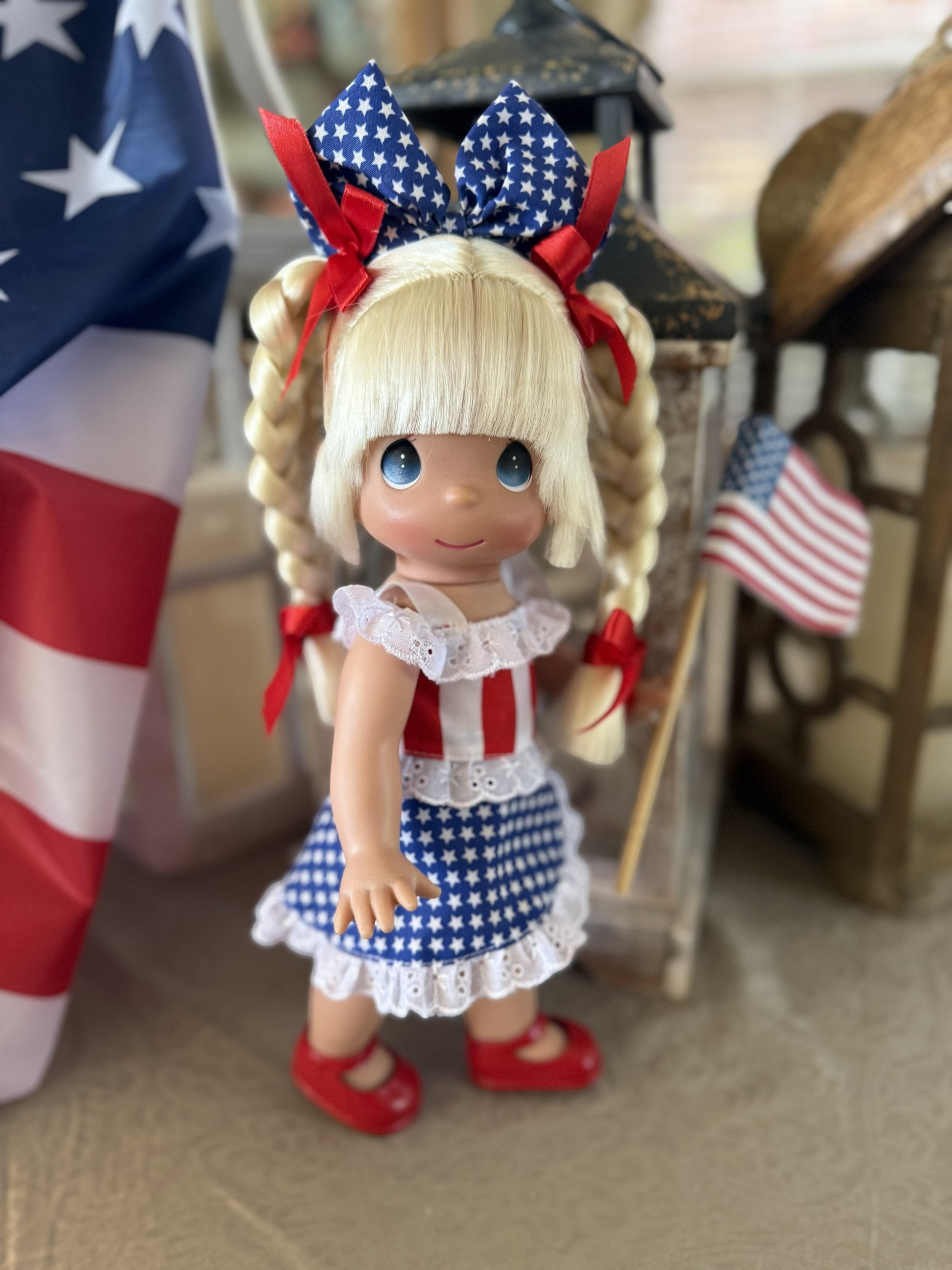The Doll Maker 12-inch Happy Birthday America doll with blonde pigtails wearing a red, white, and blue patriotic dress.