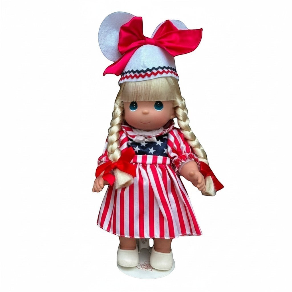The Doll Maker 12-inch blonde doll wearing a patriotic red, white, and blue striped dress with mouse ear hat