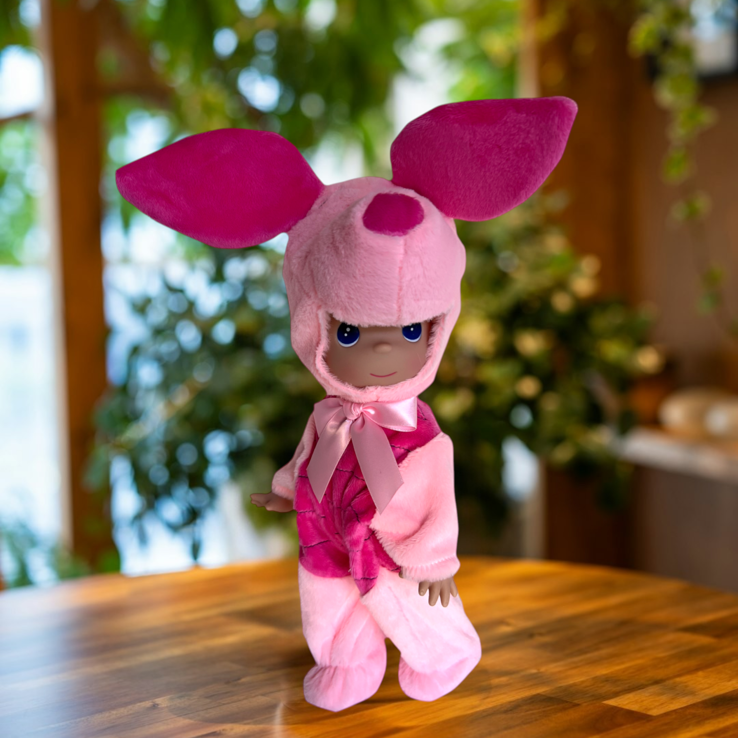 The Doll Maker 12-inch Piglet collectible doll wearing a soft pink plush hood with large ears and a satin bow.