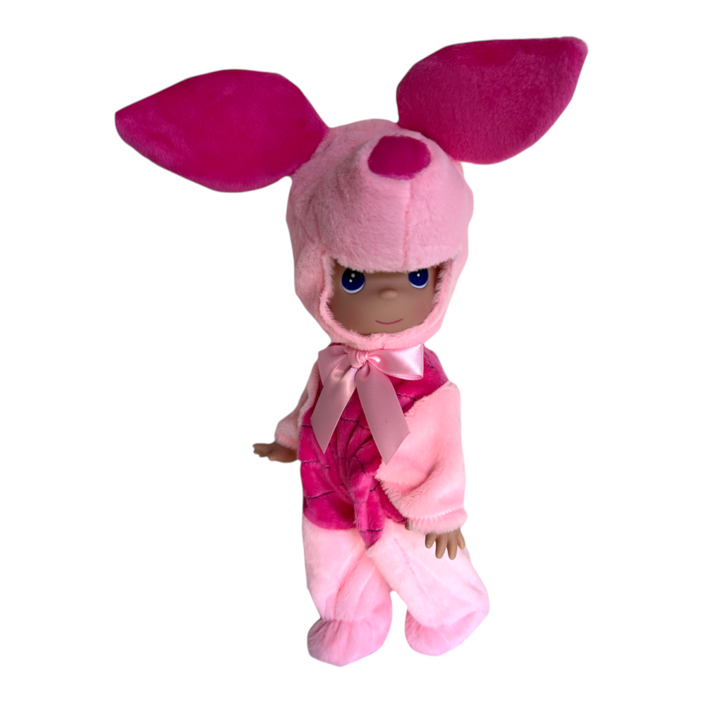 The Doll Maker 12-inch Piglet doll wearing a soft pink plush hood with large ears and a matching striped onesie.