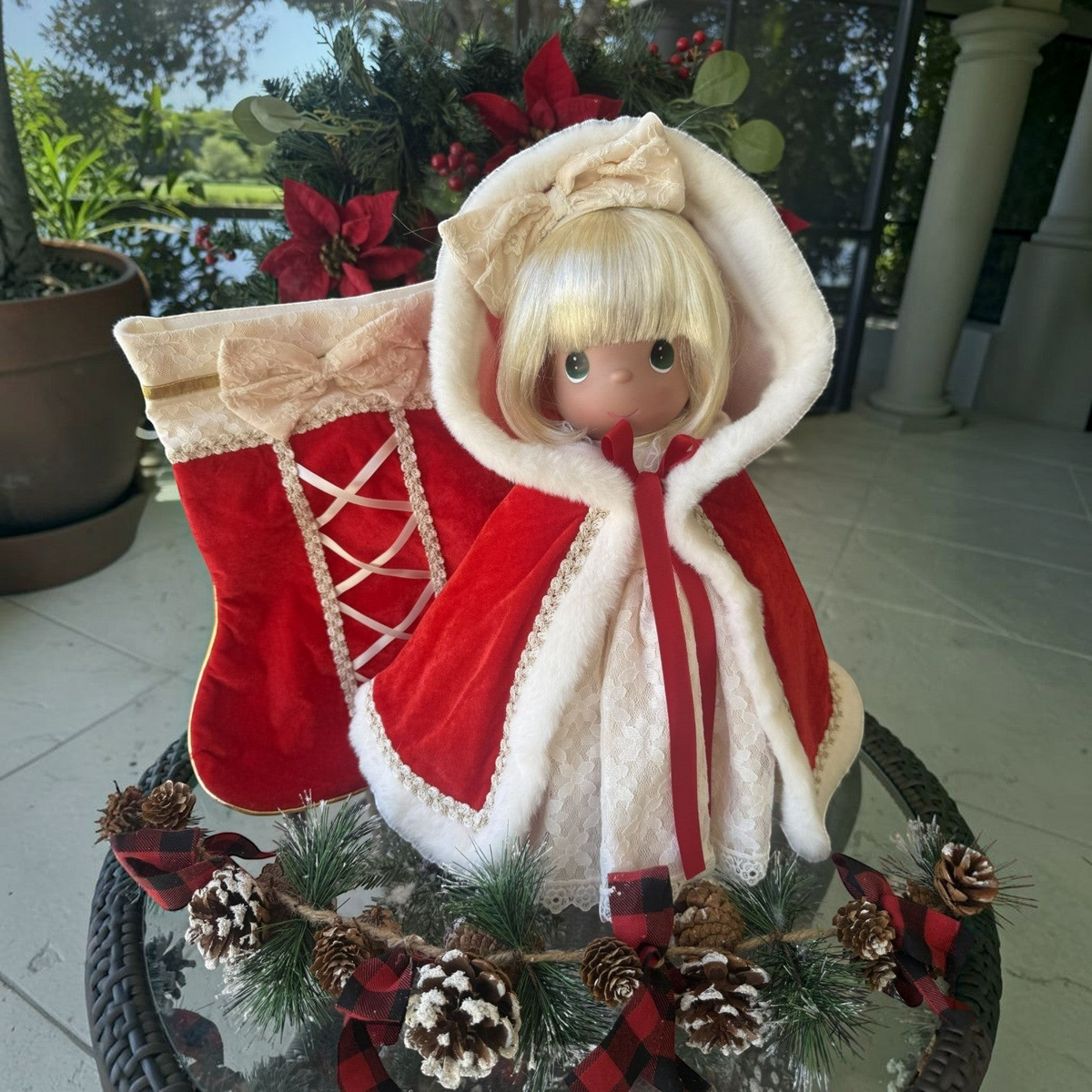 The Doll Maker 2026 Precious Moments Christmas Darling doll in a red velvet hooded cape with a matching holiday stocking