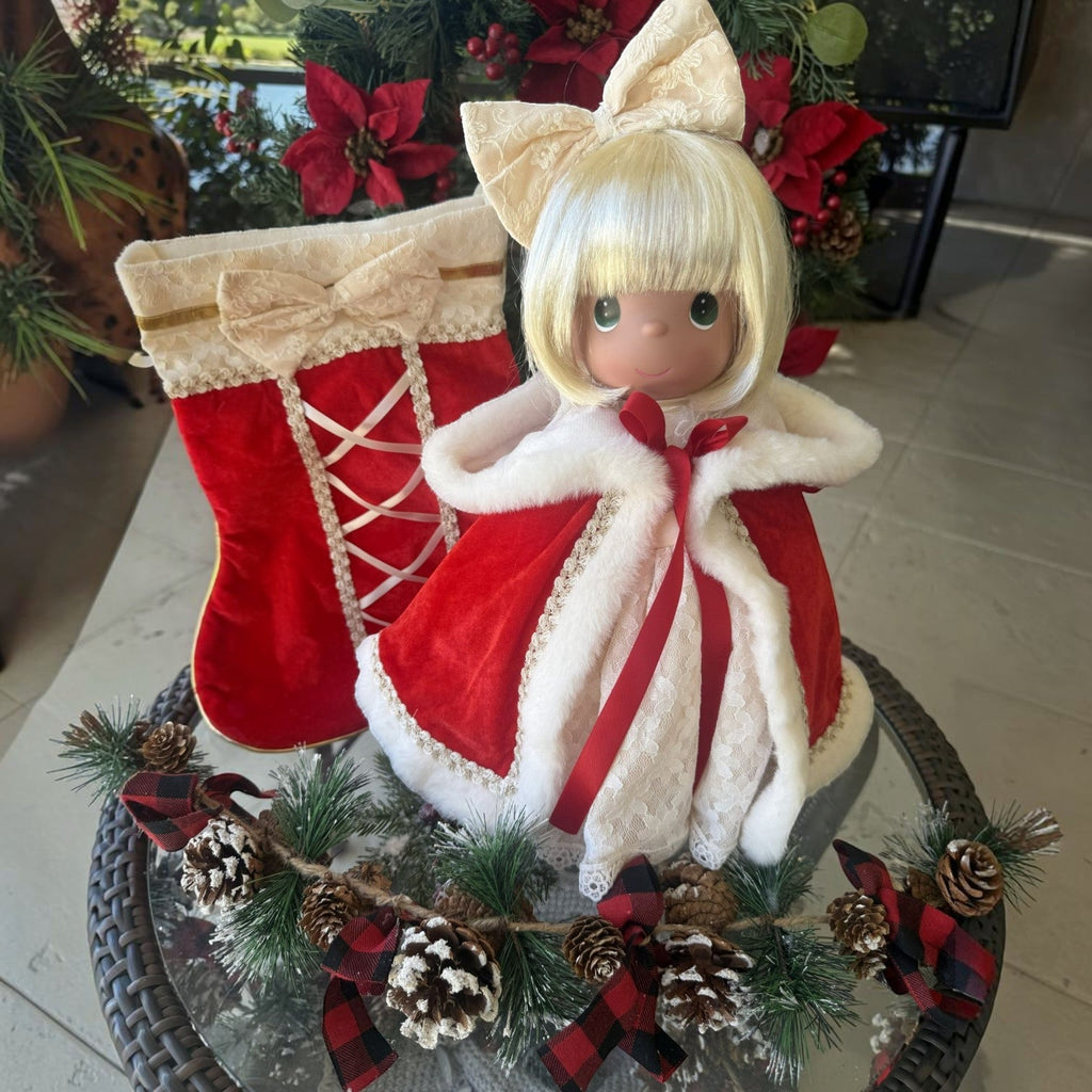 The Doll Maker Precious Moments 2026 Christmas Darling doll in a red velvet cape with a matching holiday stocking.