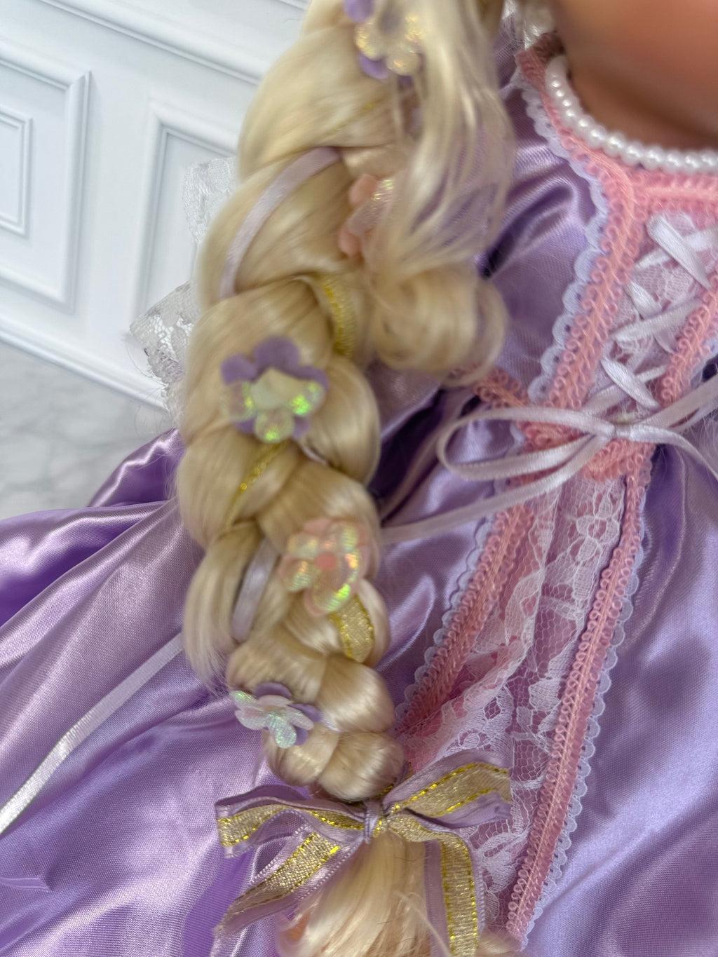 The Doll Maker 12-inch Rapunzel doll featuring a long blonde braided hairstyle decorated with small purple flowers.