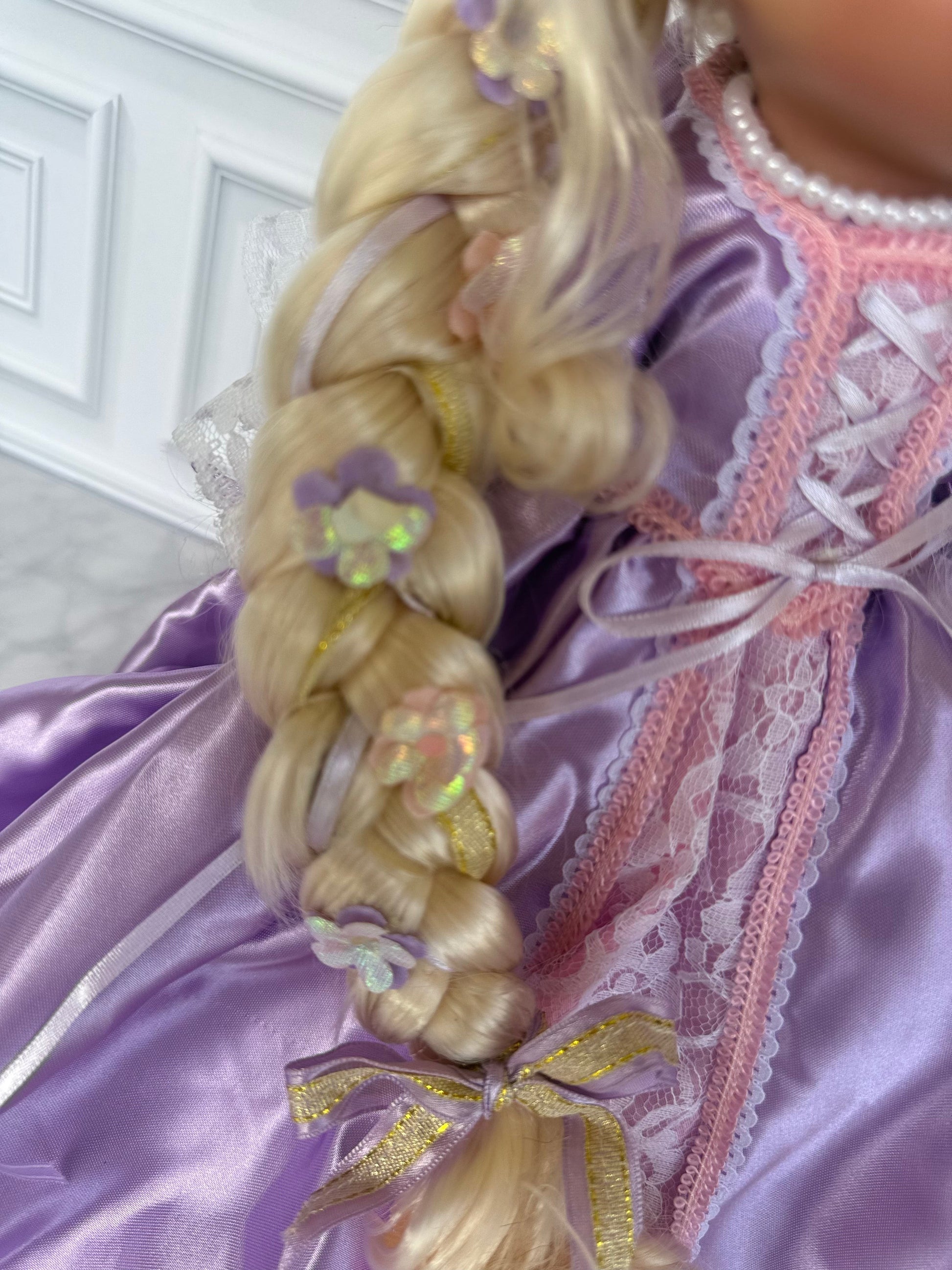 The Doll Maker 12-inch Rapunzel doll featuring a long blonde braided hairstyle decorated with small purple flowers.