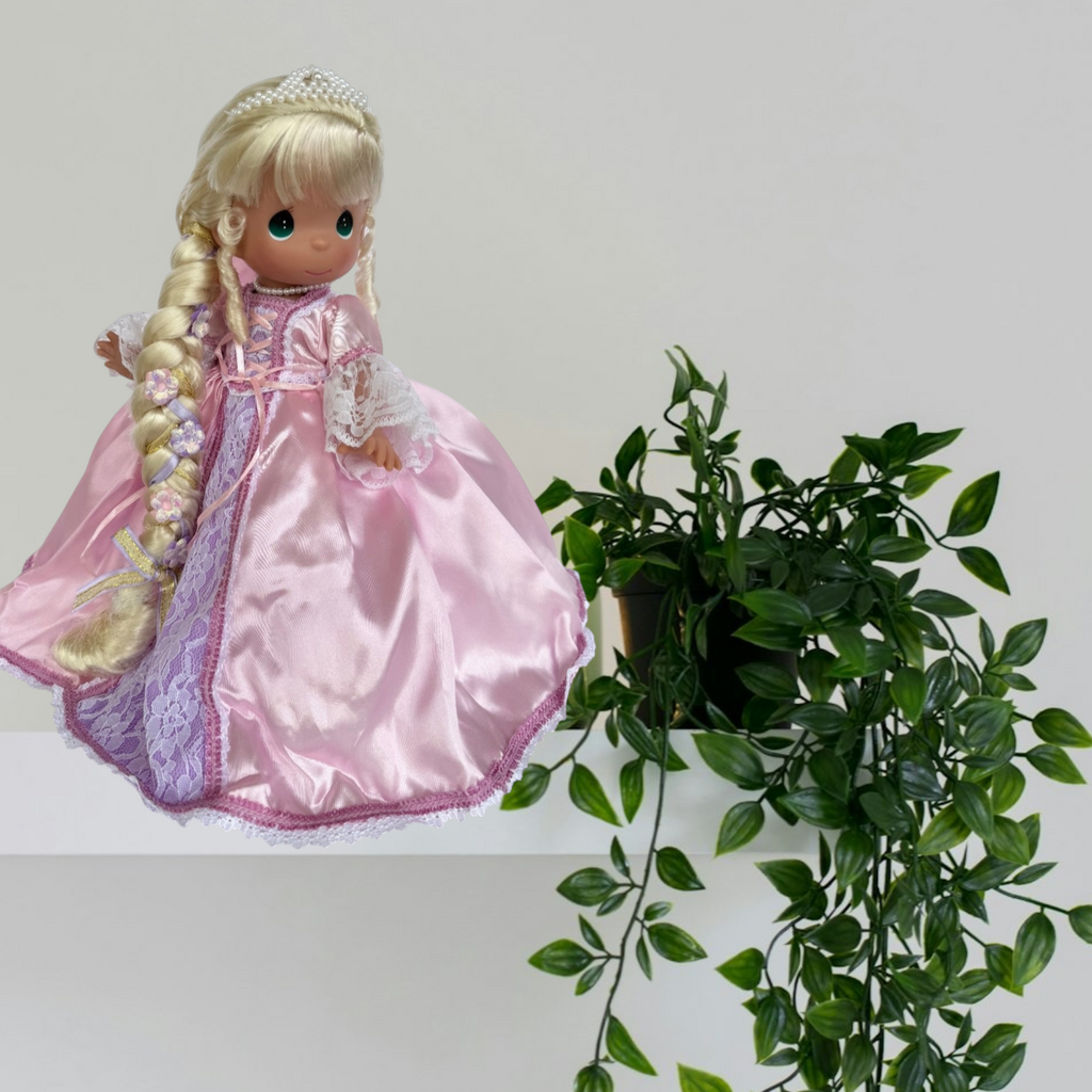 The Doll Maker 12-inch Rapunzel doll wearing a pink satin dress with lace details and long braided blonde hair.