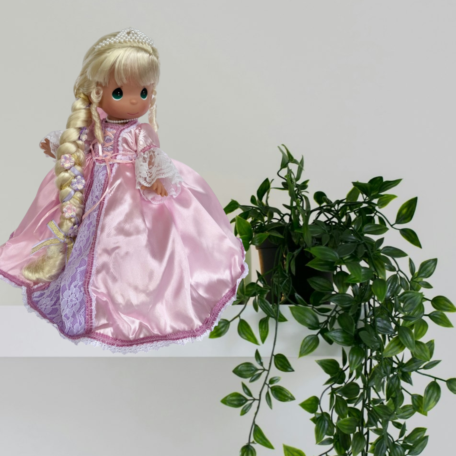 The Doll Maker 12-inch Rapunzel doll wearing a pink satin dress with lace details and long braided blonde hair.