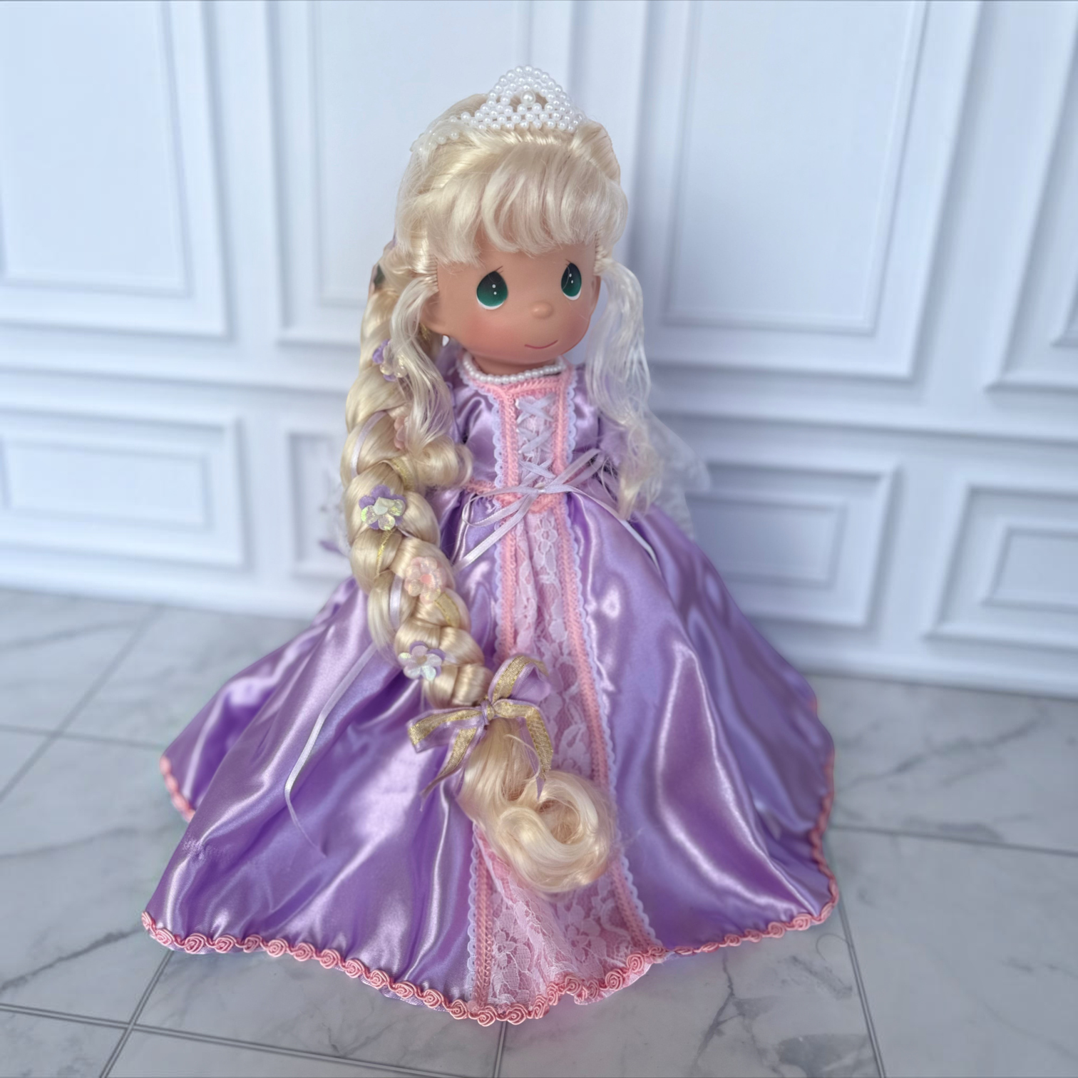 The Doll Maker 12-inch Rapunzel doll wearing a purple satin gown with lace trim, pearl tiara, and long braided hair.